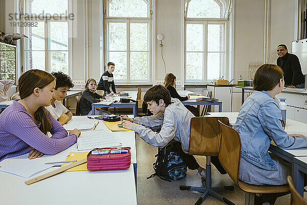 Schuljunge  der seinen Freunden hilft  auf dem Schreibtisch im Klassenzimmer zu sitzen