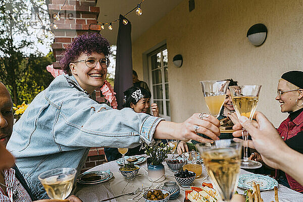 Glückliche nicht-binäre Person stößt mit Freunden bei einer Party im Hinterhof auf Getränke an