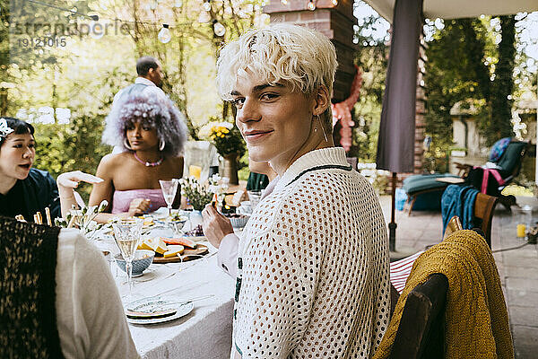 Porträt eines lächelnden schwulen Mannes mit grauem Haar  der inmitten von Freunden bei einer Dinnerparty im Hinterhof sitzt