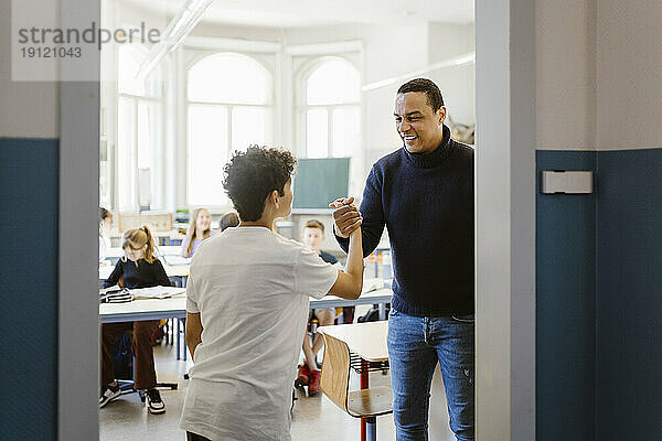 Lächelnder männlicher Lehrer beim Händeschütteln mit einem Schüler im Klassenzimmer