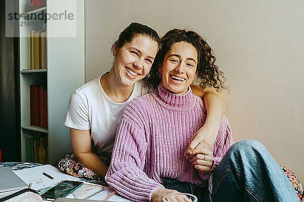 Porträt einer glücklichen jungen Frau mit einem Arm um einen Freund  der zu Hause sitzt