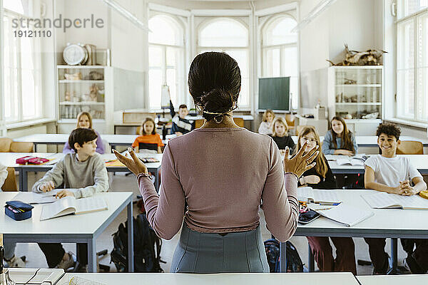 Rückansicht einer Lehrerin  die Schülern erklärt  wie sie im Klassenzimmer sitzen