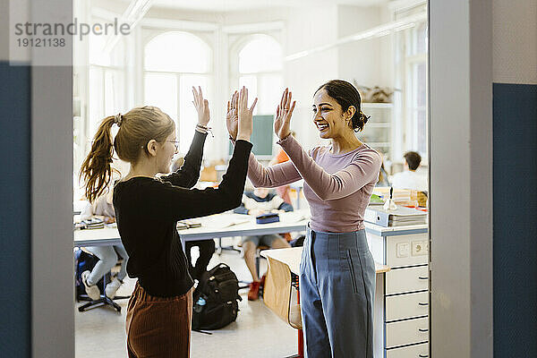 Lächelnde Lehrerin  die einem Mädchen im Klassenzimmer die Hand drückt