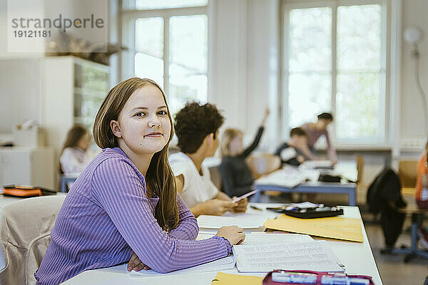 Porträt einer lächelnden Schülerin am Schreibtisch im Klassenzimmer