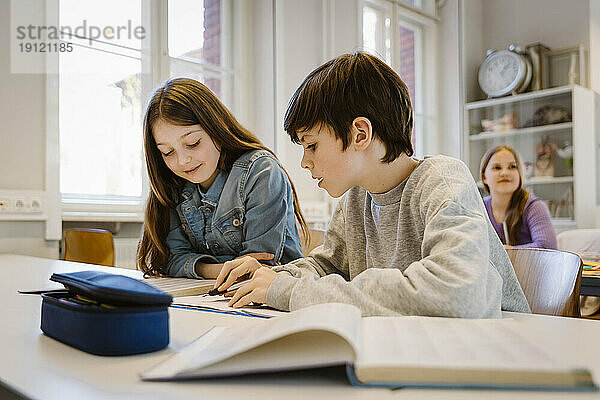 Junge hilft seiner Freundin beim gemeinsamen Lernen am Schreibtisch im Klassenzimmer