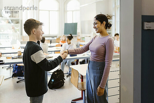 Lächelnder Lehrer  der einem Schüler im Klassenzimmer die Hand schüttelt