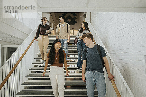 Fröhliche multirassische Studentinnen und Studenten  die sich auf den Stufen der Universität nach unten bewegen
