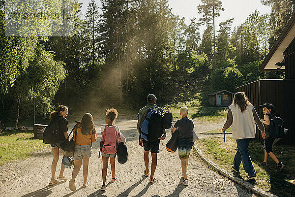 Rückansicht von Kindern  die mit Betreuern im Sommercamp auf dem Fußweg gehen