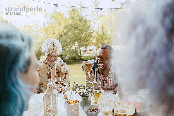 Glückliche schwule Freunde lachen  während sie mit Freunden während einer Dinnerparty im Hinterhof etwas trinken
