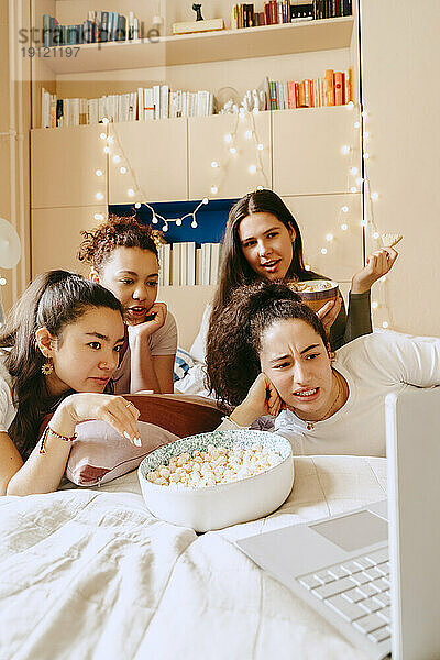 Gemischtrassige Freunde sehen sich zu Hause gemeinsam einen Film auf dem Laptop an