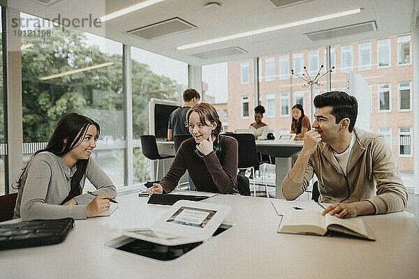 Glückliche männliche und weibliche Studenten verschiedener Rassen  die an einem Tisch in der Universität lernen