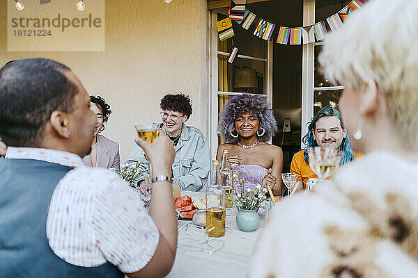 Lächelnde Freunde der LGBTQ-Gemeinschaft genießen Wein bei einer Dinnerparty im Hinterhof