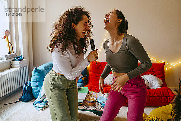 Verspielte junge Frauen genießen die Musik beim Singen zu Hause