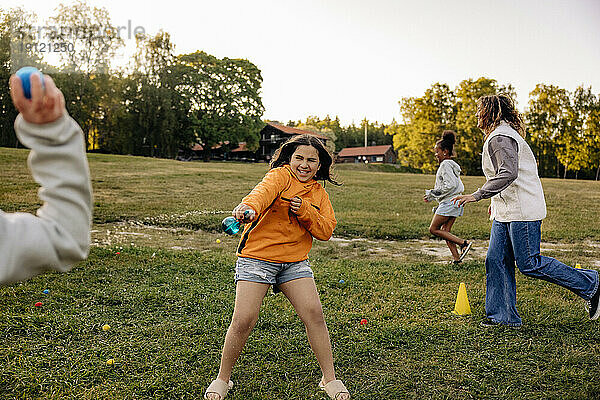 Fröhliches Mädchen spritzt mit Wasser  während es mit Freunden auf dem Spielplatz im Sommercamp spielt