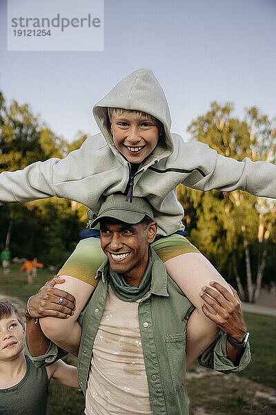 Männlicher Betreuer trägt einen Jungen auf den Schultern  während er auf dem Spielplatz Spaß hat