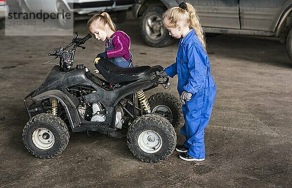 Zwei kleine Mädchen in Overalls inspizieren ein Quad