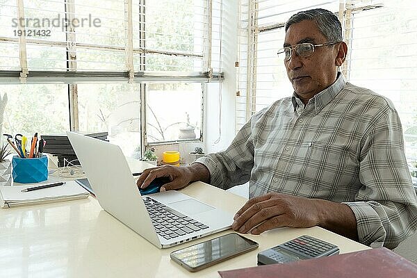 Älterer hispanischer Mann  der einen Laptop für geschäftliche Zwecke benutzt. Textfreiraum