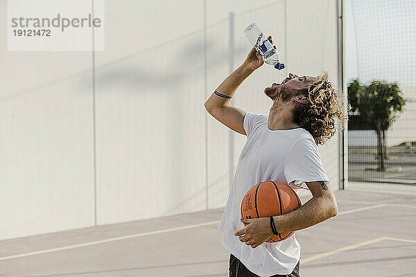 Seitenansicht junger Mann mit Basketball  der Wasser trinkt