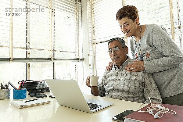Älterer Mann und seine Frau schauen auf einen Laptop. Sie führen einen Videoanruf  lächeln und sehen entspannt aus
