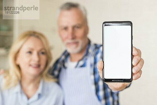 Unscharfes Portrait eines älteren Paares  das ein Mobiltelefon mit weißem Bildschirm hält