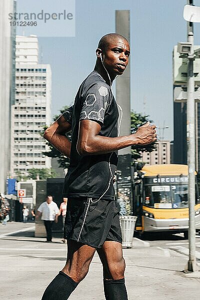 Selbstbewusster männlicher Athlet fitter junger Männchen joggt auf der Straße und hört Musik über Kopfhörer