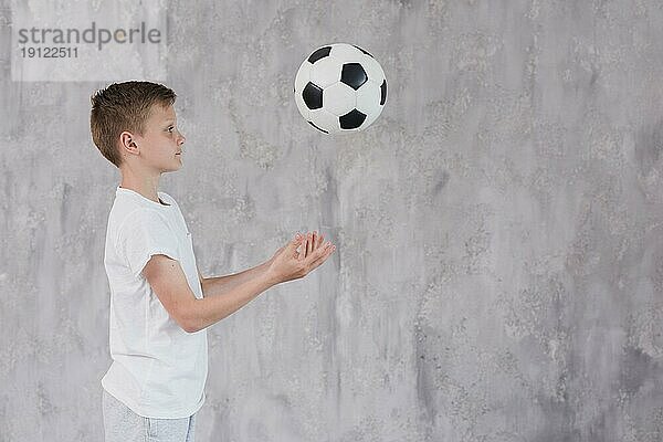 Seitenansicht Junge spielt mit Fußball gegen Betonkulisse