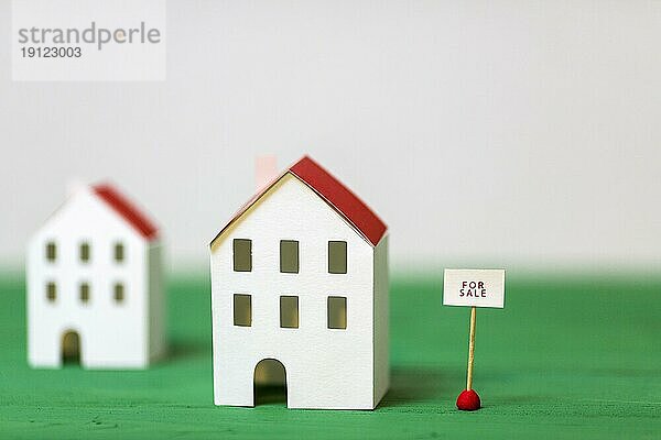Miniatur Haus Modell in der Nähe von Verkauf Tag grün texturierten Schreibtisch vor weißem Hintergrund