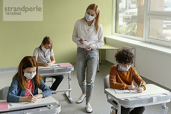 Kinder mit medizinischen Masken lernen in der Schule mit einem Lehrer
