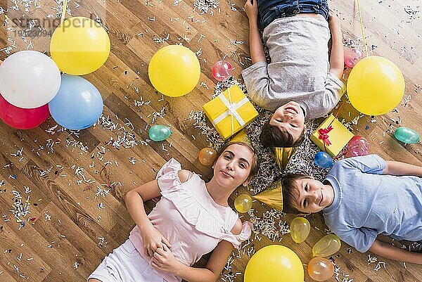 Overhead Ansicht glücklich Geschwister liegen mit Luftballons Geschenkbox Konfetti Boden
