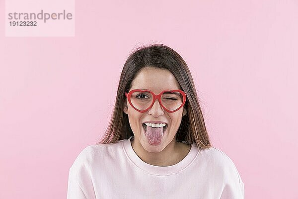 Junge glückliche Frau mit Brille zeigt Zunge