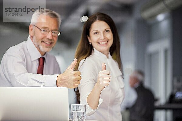 Lächelnde erfolgreiche Geschäftsleute mit Daumen nach oben Zeichen Büro