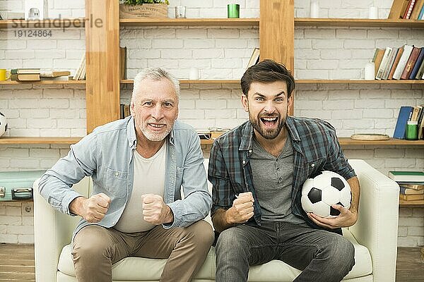 Älterer Mann junger weinender Mann mit Ball vor dem Fernsehsofa