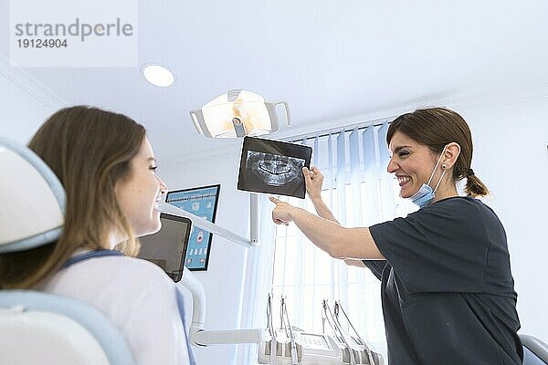 Glücklich lächelnde Zahnärztin  die einen Patienten mit Röntgenstrahlen zeigt