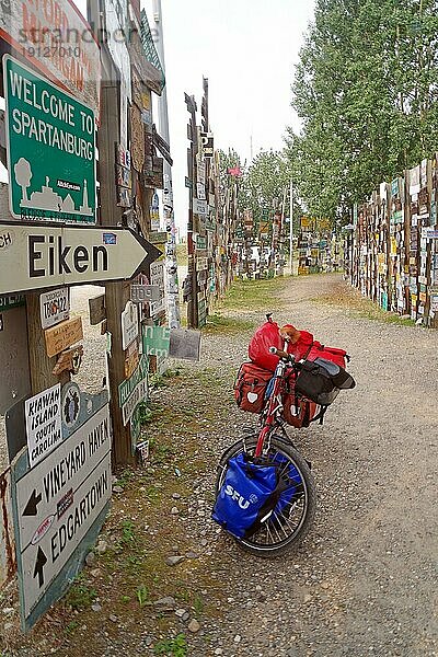 Verschiedene Verkehrs- und Ortschilder stehen einem mit Gepäck beladenem Fahrrad  Schilderwald  Abenteuerreise  Watson Lake  Yukon Territory  Kanada  Nordamerika