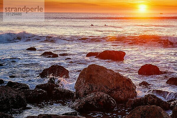 Sonnenuntergang über dem Atlantik mit Wellen und Felsen und Surfer Silhouetten im Wasser an der Costa da Caparica  Portugal  Europa