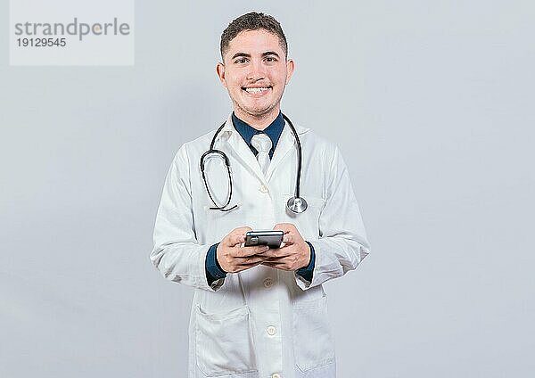 Glücklicher lateinischer Arzt  der ein Telefon hält  isoliert. Fröhlich Arzt mit Handy Blick in die Kamera isoliert