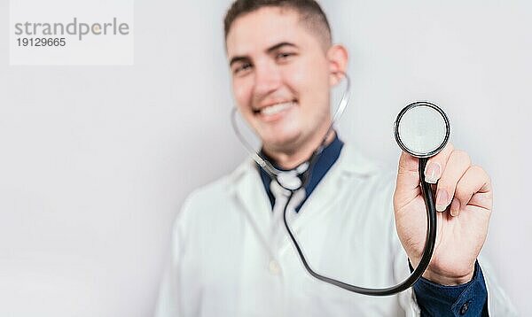 Glücklicher junger Arzt  der ein Stethoskop hält und in die Kamera schaut. Porträt eines lateinischen Arztes  der ein Stethoskop hält  isoliert