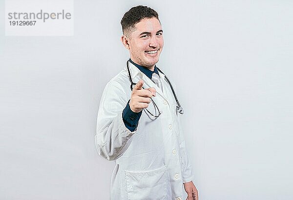 Hübscher Arzt  der auf die Kamera zeigt. Freundlicher und lächelnder Arzt  der auf Sie zeigt  Junger Arzt