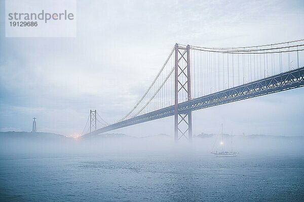 Blick auf die Brücke 25 de Abril  das berühmte touristische Wahrzeichen Lissabons  die Lisboa und Almada verbindet  im dichten Nebel mit darunter durchfahrenden Booten. Lissabon  Portugal  Europa