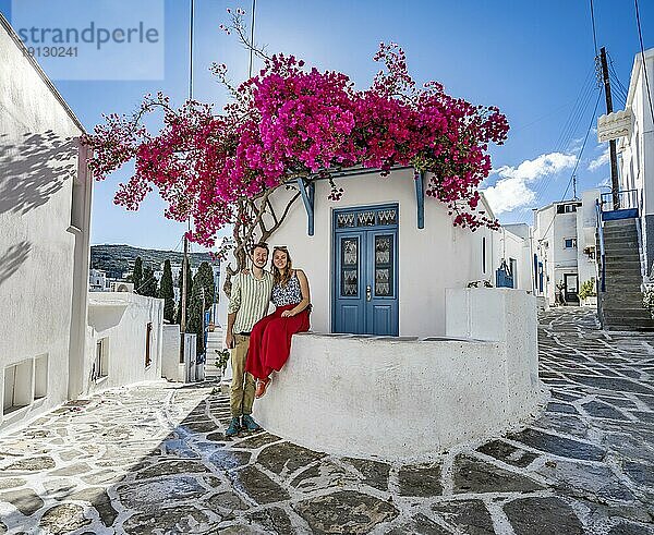 Junges verliebtes Paar  weißes kykladisches Haus mit blauer Tür und rosa Bougainvillea  mit Sonnenstern  malerische Gassen des Ortes Lefkes  Paros  Kykladen  Griechenland  Europa