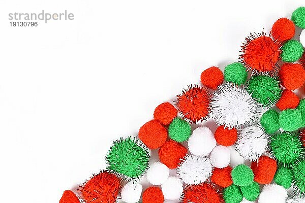 Flauschige runde Pompons in traditionellen Weihnachtsfarben rot  grün und weiß in der Ecke des weißen Hintergrunds mit leeren Kopierraum