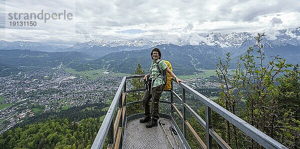 Bergsteigerin auf einer Aussichtsplattform  Ausblick über den Ort Garmisch-Partenkirchen mit wolkenverhangenen Bergen des Wettersteingebirges  Ammergauer Alpen  Bayern  Deutschland  Europa