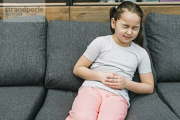 Porträt Mädchen sitzt grau Sofa mit schweren Schmerzen Magen