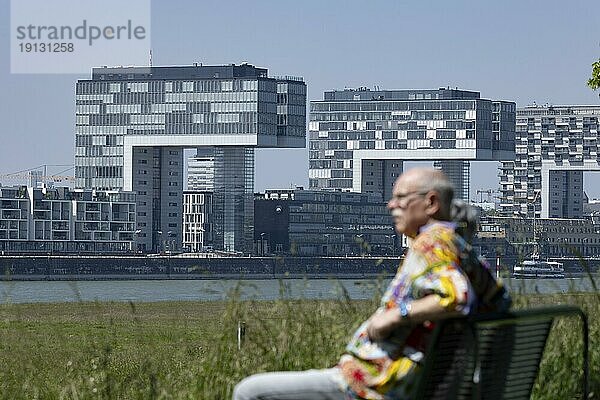 Seniorenpaar sitzt auf einer Bank am Rheinufer vor den Kranhäusern im Kölner Rheinauhafen am anderen Ufer  Köln  Nordrhein-Westfalen  Deutschland  Europa