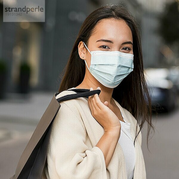 Frau mit medizinischer Maske beim Einkaufsbummel mit Einkaufstasche