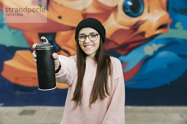 Glückliche Frau hält Sprühflasche vor Graffitiwand