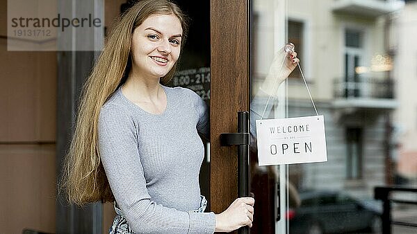 Lächelnde Frau  die ein offenes Schild an der Tür eines Cafés anbringt