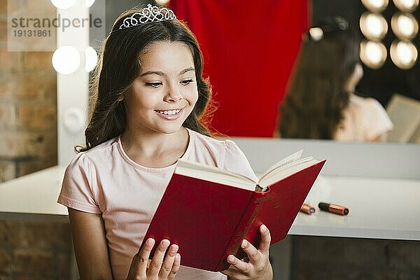 Lächelndes Mädchen sitzt im Schminkraum und liest ein Buch