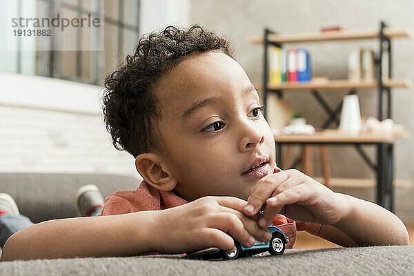 Nachdenklicher schwarzer Junge spielt mit Spielzeugauto