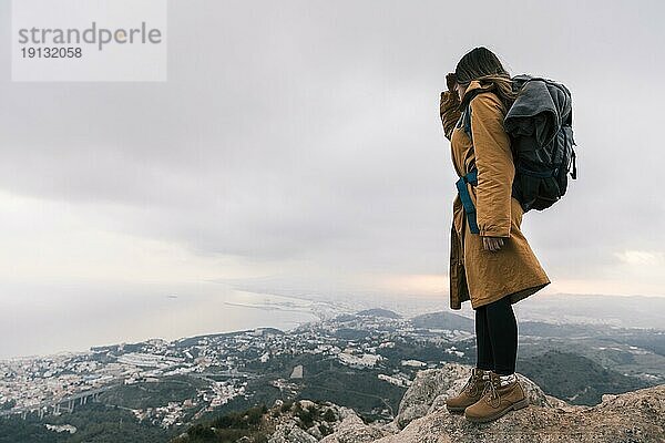 Junge Frau mit Rucksack auf dem Gipfel eines Berges mit idyllischer Aussicht
